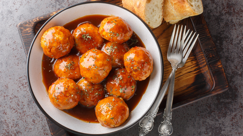 Sweet and sour meatballs in spicy sauce in a white bowl with two forks and chunks of bread