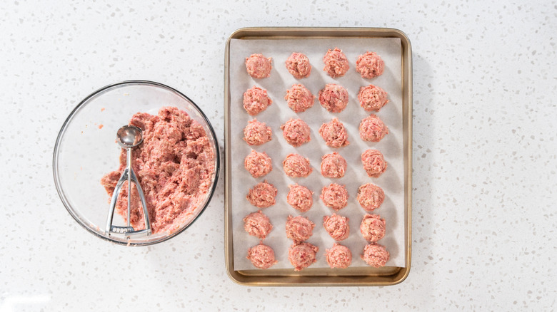 Forming meatballs with an ice cream scooper and placing them on baking sheet