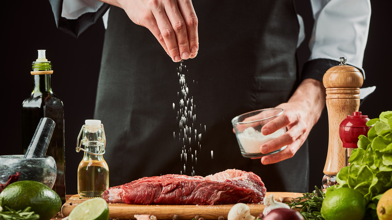 chef sprinkling salt high above steak