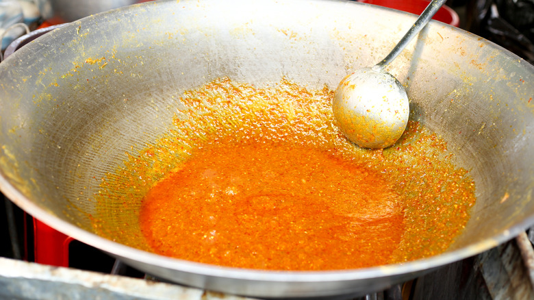 Large wok, with orange curry sauce being stirred with ladle