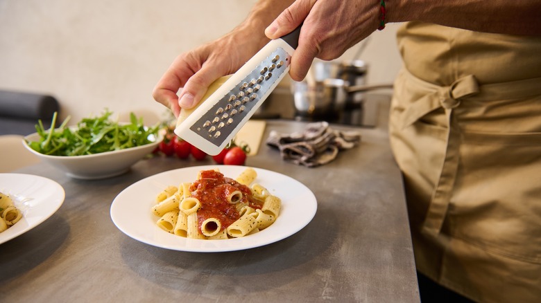 Person grating Parmesan onto plate of pasta