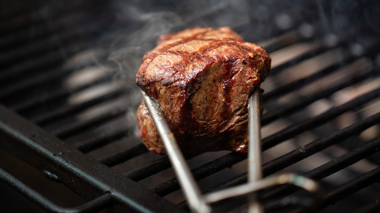 Tongs squeezing seared steak