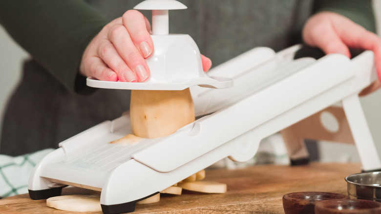 Person slicing potatoes on mandoline with hand guard