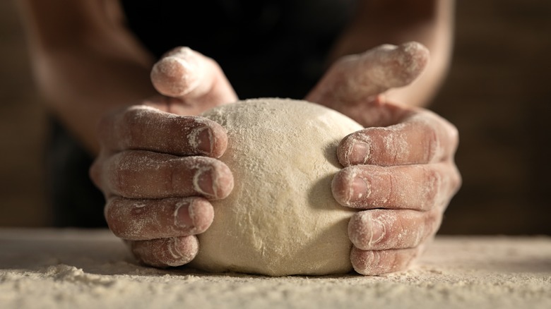 Flour-covered hands holding pizza dough