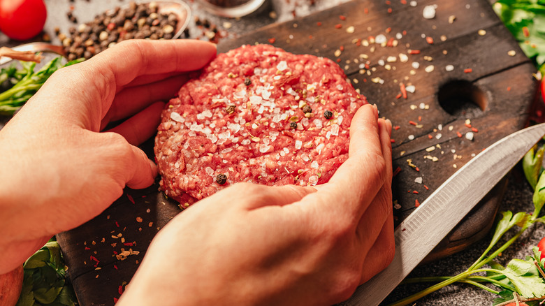 Hands seasoning burger patty with salt