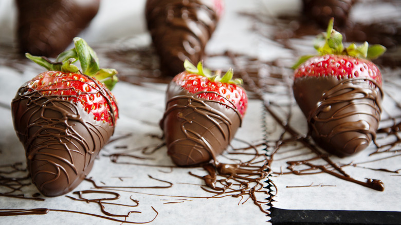 strawberries dipped in and drizzled with temered chocolate sitting on parchment paper