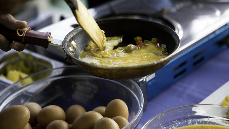 Hands mixing scrambled eggs in pan