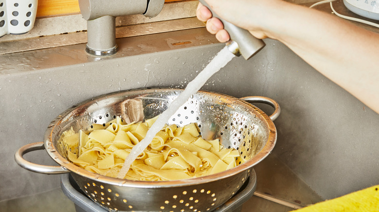 rinsing cooked pasta in a colander with cold water