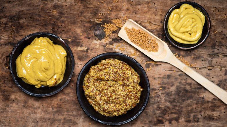 Assorted mustards in dishes on wooden background