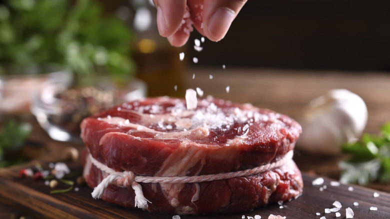 person salting raw meat