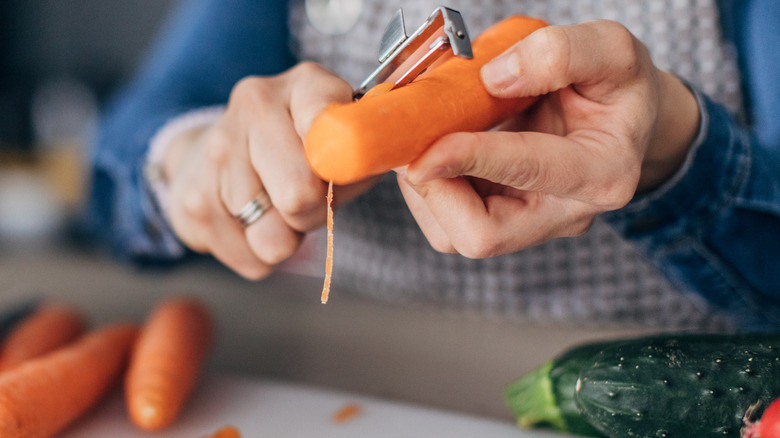 person peeling carrot with vegetable peeler