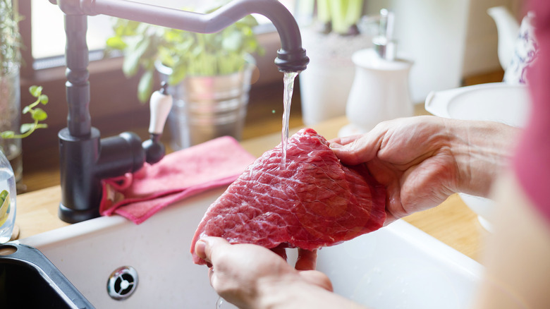 An individual washing red meat steak