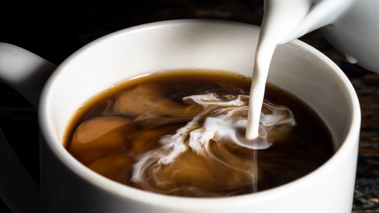 A person pours milk into their coffee