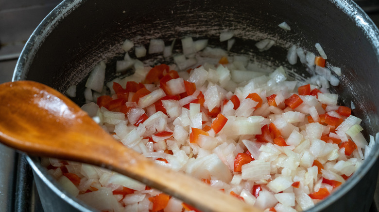 Diced onions and tomatoes in a pan with a wooden spoon