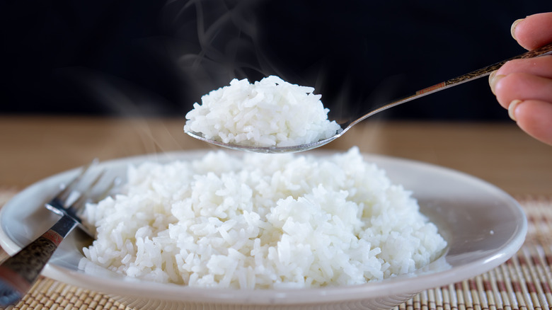 person spooning steaming white rice off a place