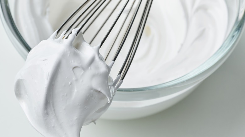 Whipped cream on a whisk over a glass bowl