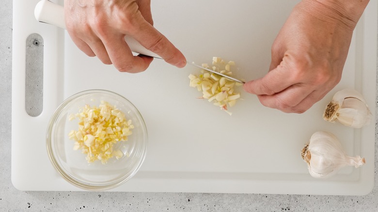 garlic being minced with knife on white chopping board