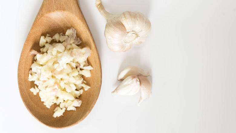 minced garlic on wooden spoon next to unpeeled cloves