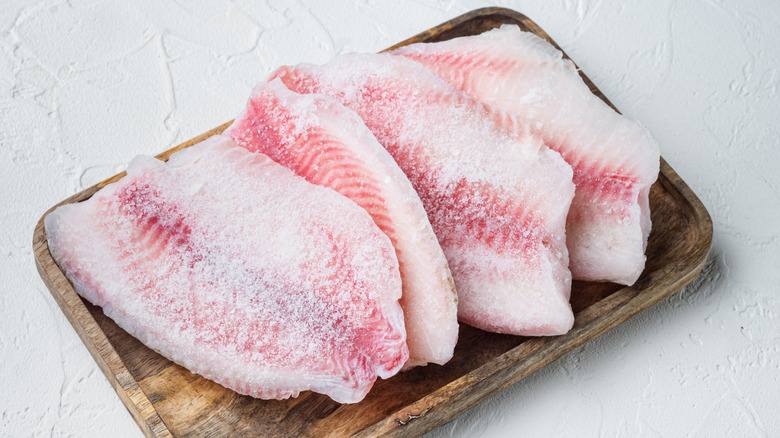 Frozen fish filets on wooden board with white textured background