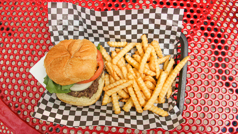 Fast food burger and fries in a basket with retro-style checkered wax paper on a red picnic table