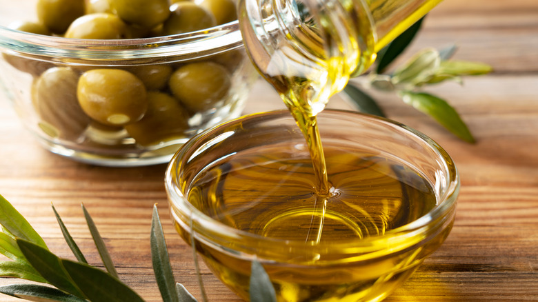 Golden olive oil being poured into a glass dish