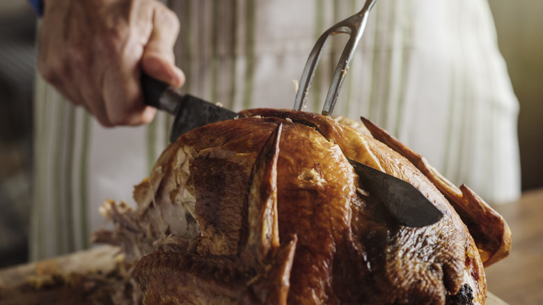 Someone cutting a roasted turkey with a knife and fork