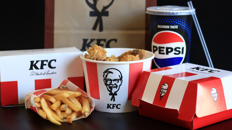 A spread of boxed KFC food, including an open bucket of wings and bag of french fries