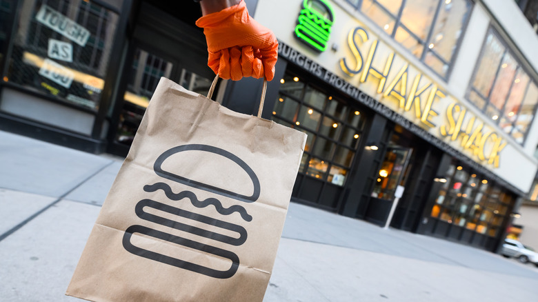 Orange gloved hand holding a brown Shake Shack bag