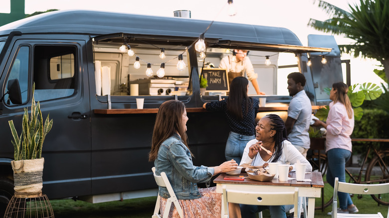 Two women dining in front of a black food truck