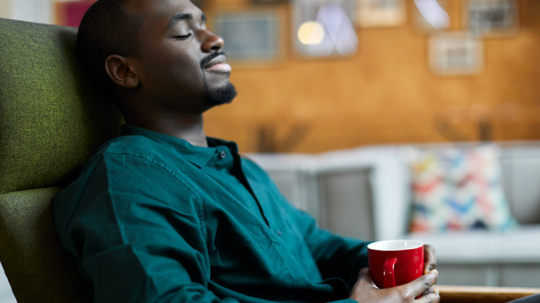 man with eyes closed holding coffee cup