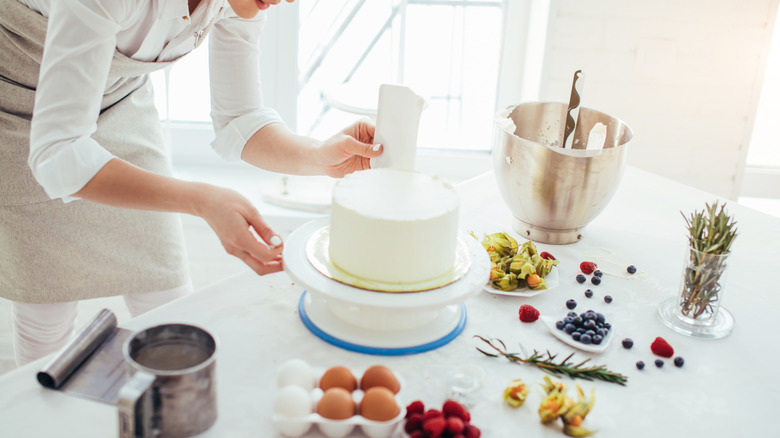 baker using bench scraper on cake in kitchen