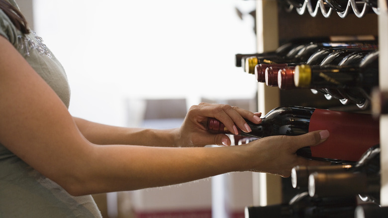 woman taking a bottle of wine out of a storage rack