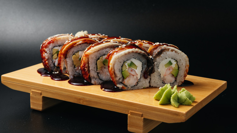 A sushi roll on a wooden board with wasabi.