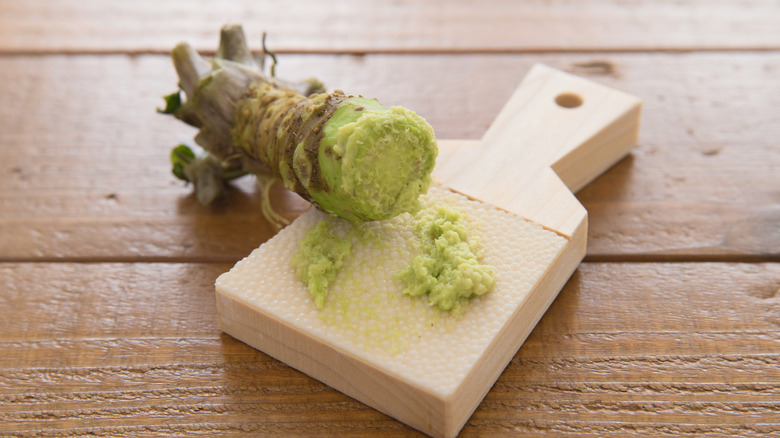 Wasabi root partially grated on a wooden board.