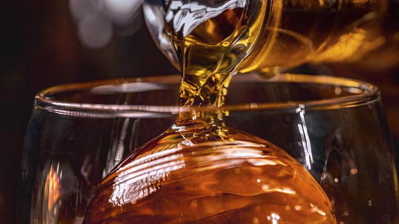 Liquor being poured on an ice sphere in a glass