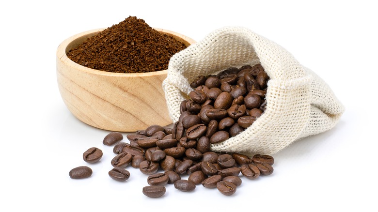 A wooden bowl of coffee powder on the left and a sack of coffee beans on the right