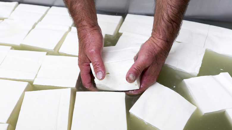 hands pulling feta cheese from brine