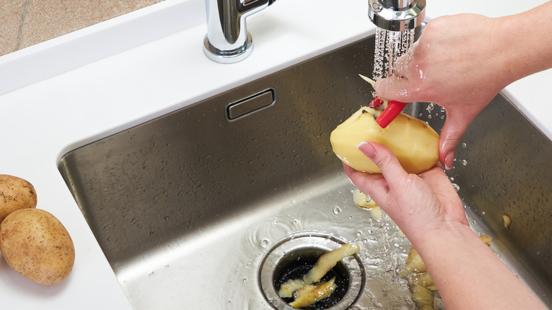 peeling potatoes over kitchen sink