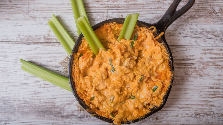 skillet with Buffalo chicken dip and celery on wood table