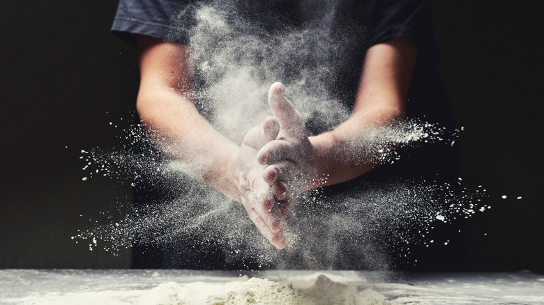 A baker clapping their hands together and creating a cloud of flour dust.