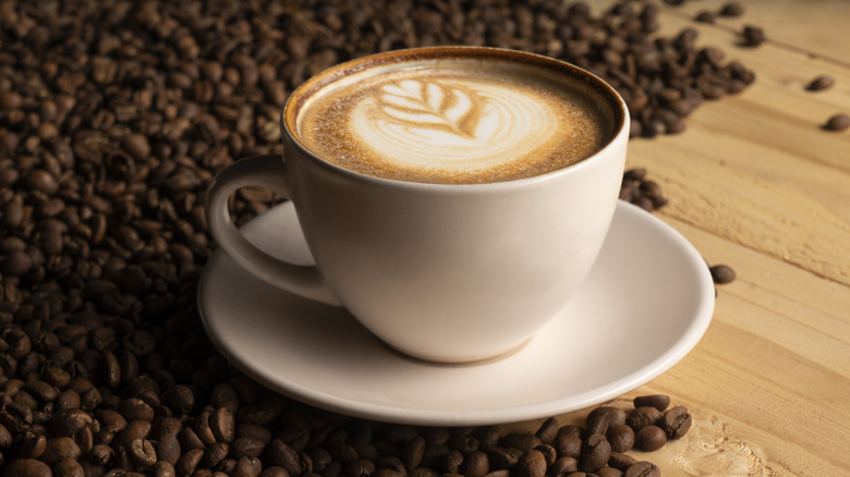 a cappucino surrounded by roasted coffee beans on rustic wood table