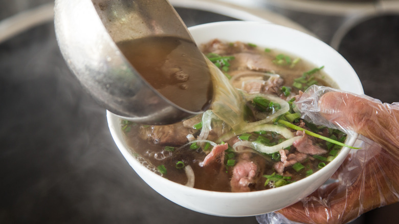 pouring broth over pho