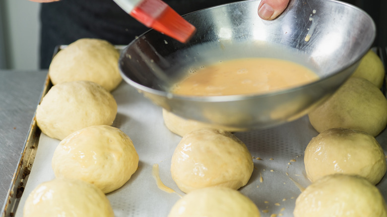 Using a pastry brush to apply egg wash to buns