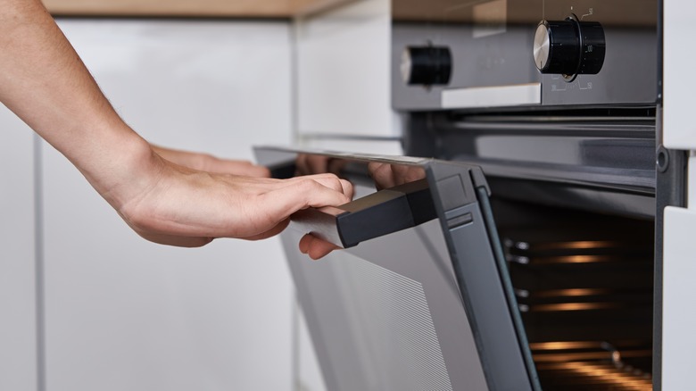 Hands opening oven, oven slightly ajar