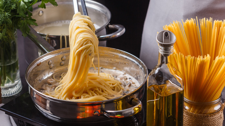 spaghetti added to cream sauce in pan