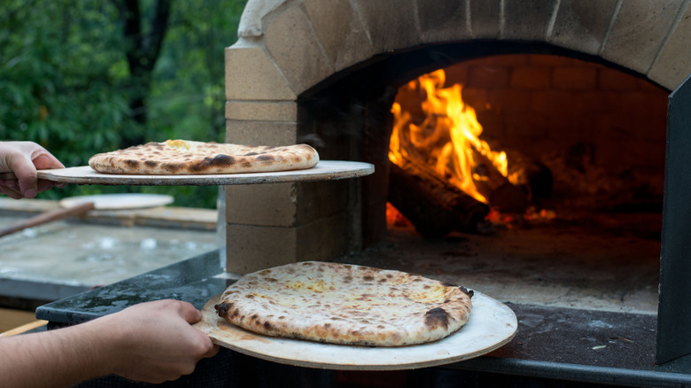 hands holding pizzas outside of a pizza oven