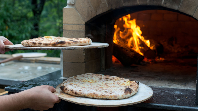 hands holding pizzas outside of a pizza oven