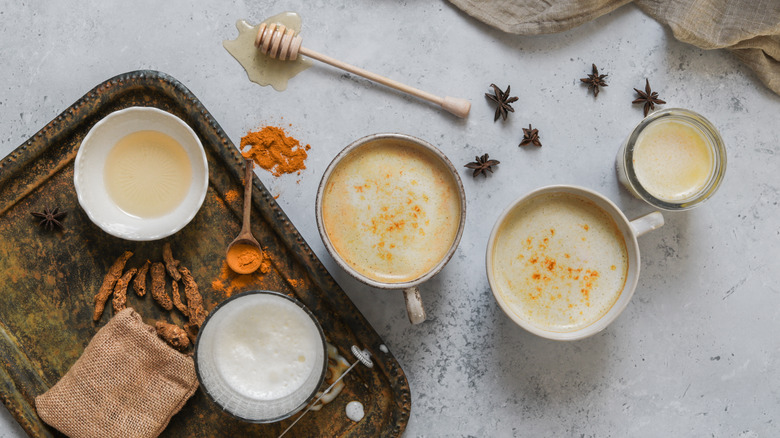 mugs of chai next to milk, honey and spices