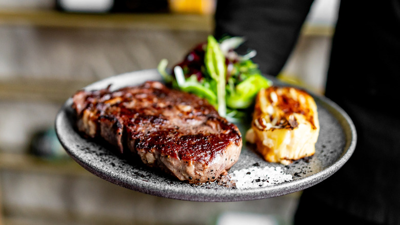 server holding a plate with steak dinner