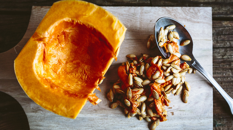 Scooped out chunk of pumpkin with its seeds and a spoon of a wooden board